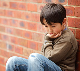 Troubled child looking sad leaning against a brick wall.